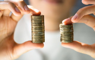 Close-up di due mani che tengono due pile di monete di altezza diversa, simbolo di disparità salariale e disuguaglianza economica.